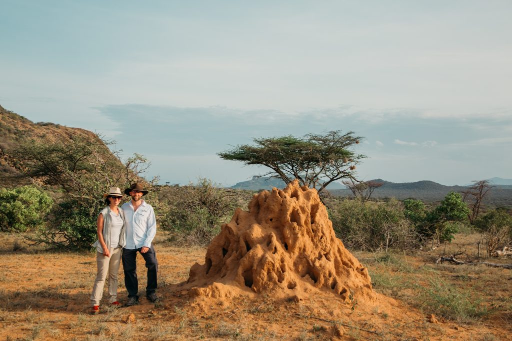 Lindsey and Zac of Have Clothes, Will Travel standing next to a massive termite hill in Samburu, Kenya