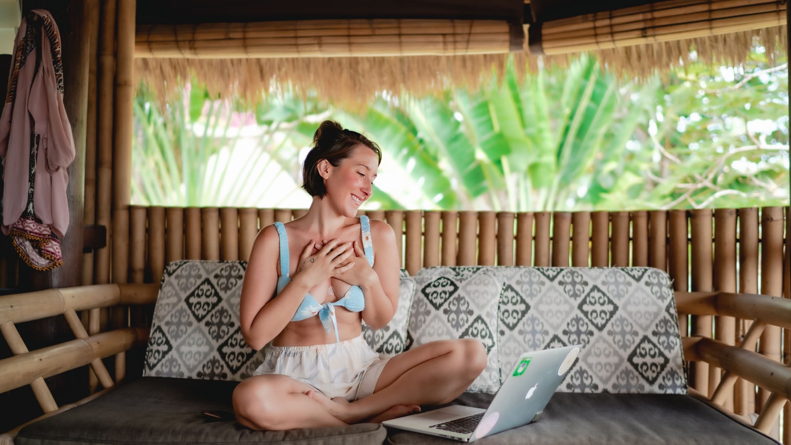 cheerful caucasian young woman talking via video calling using a laptop and wi-fi while sitting in a cozy hotel resort during a vacation