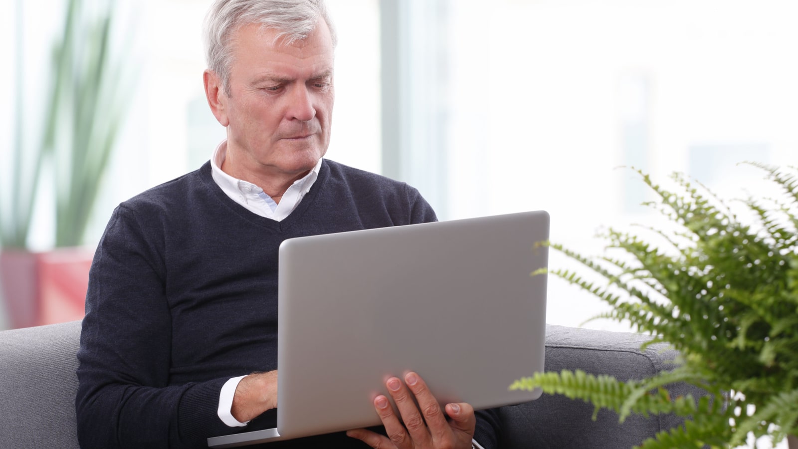 Portrait of retired casual man sitting at home and working online on laptop.