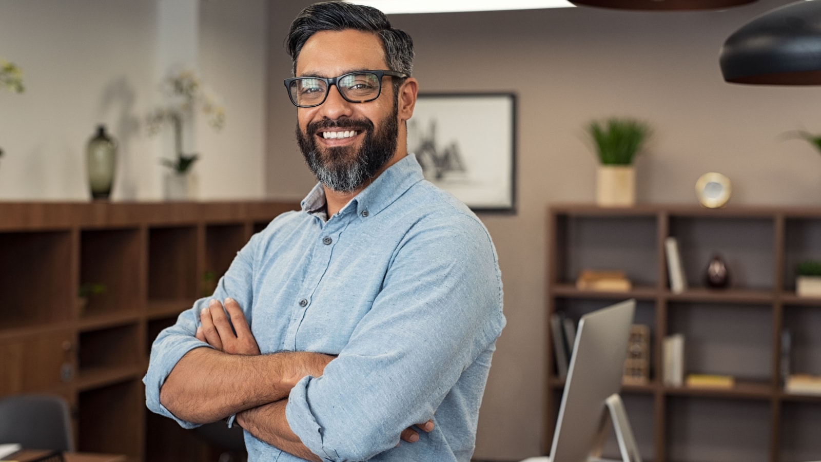 Portrait of happy mature businessman wearing spectacles and looking at camera. Multiethnic satisfied man feeling confident in a creative office. Successful middle eastern business man smiling.