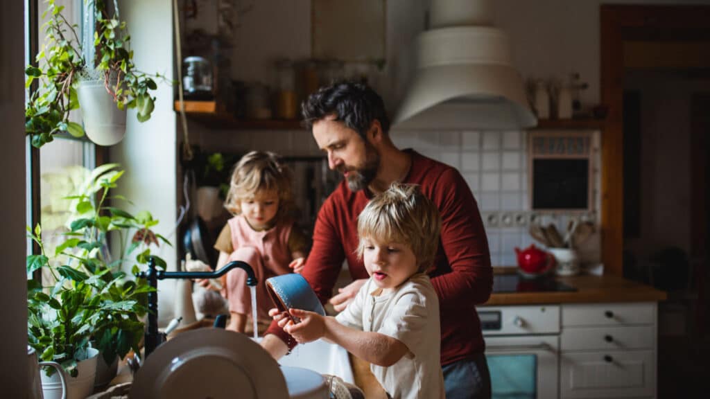 Mature father with two small children washing dishes indoors at home, daily chores concept.