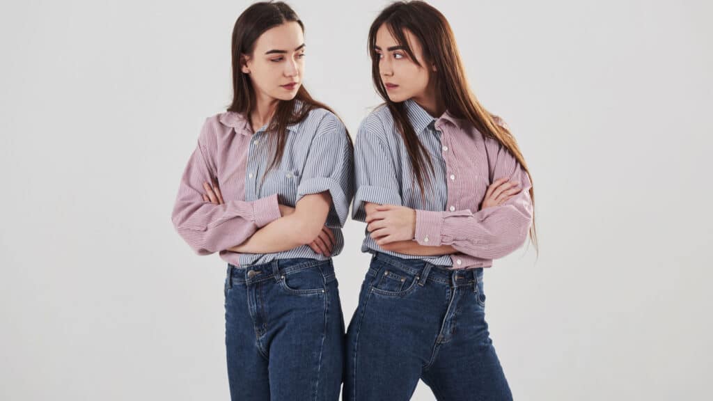 Offended and look at other with anger. Two sisters twins standing and posing in the studio with white background.