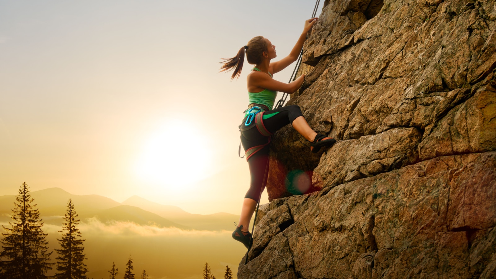 Beautiful Woman Climbing on the High Rock at Foggy Sunset in the Mountains. Adventure and Extreme Sport Concept