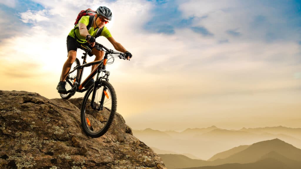 Cyclist Riding the Bike Down the Rock at Sunrise in the Beautiful Mountains on the Background. Extreme Sport and Enduro Biking Concept.