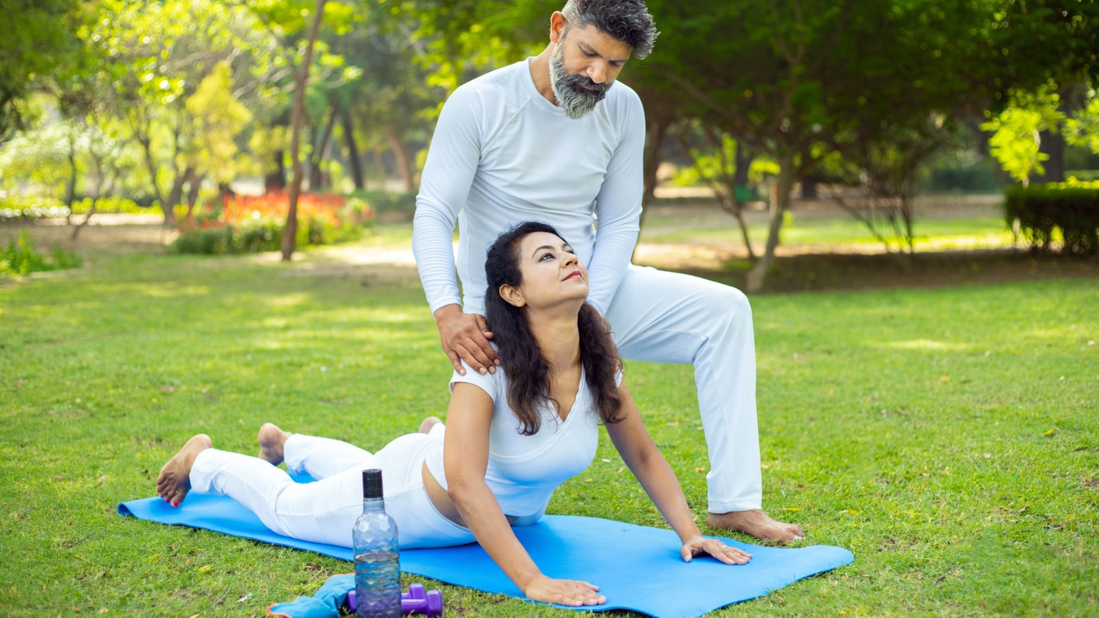 Indian male teacher or trainer teach yoga to young female student in the park, Two people do stretching fitness exercise together outdoor, Sports and workout concept.