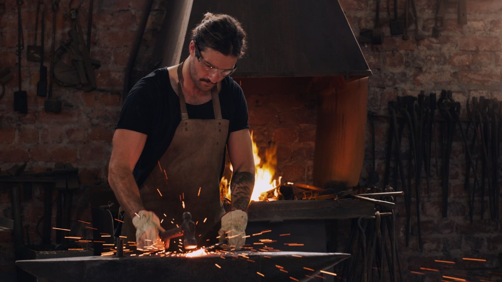 Hammer, anvil and fire with a man working in a forge for metal work manufacturing or production. Industry, welding and trade with a male blacksmith at work in a factory, plant or industrial workshop