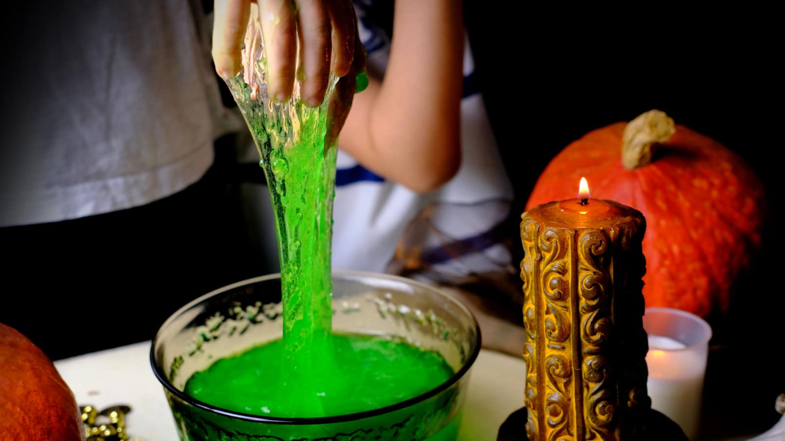 children play with a green witchcraft potion, table is covered with a black cloth, pumpkins lie, animal skulls, candles are burning, the concept of the Halloween holiday, love spell, children's party