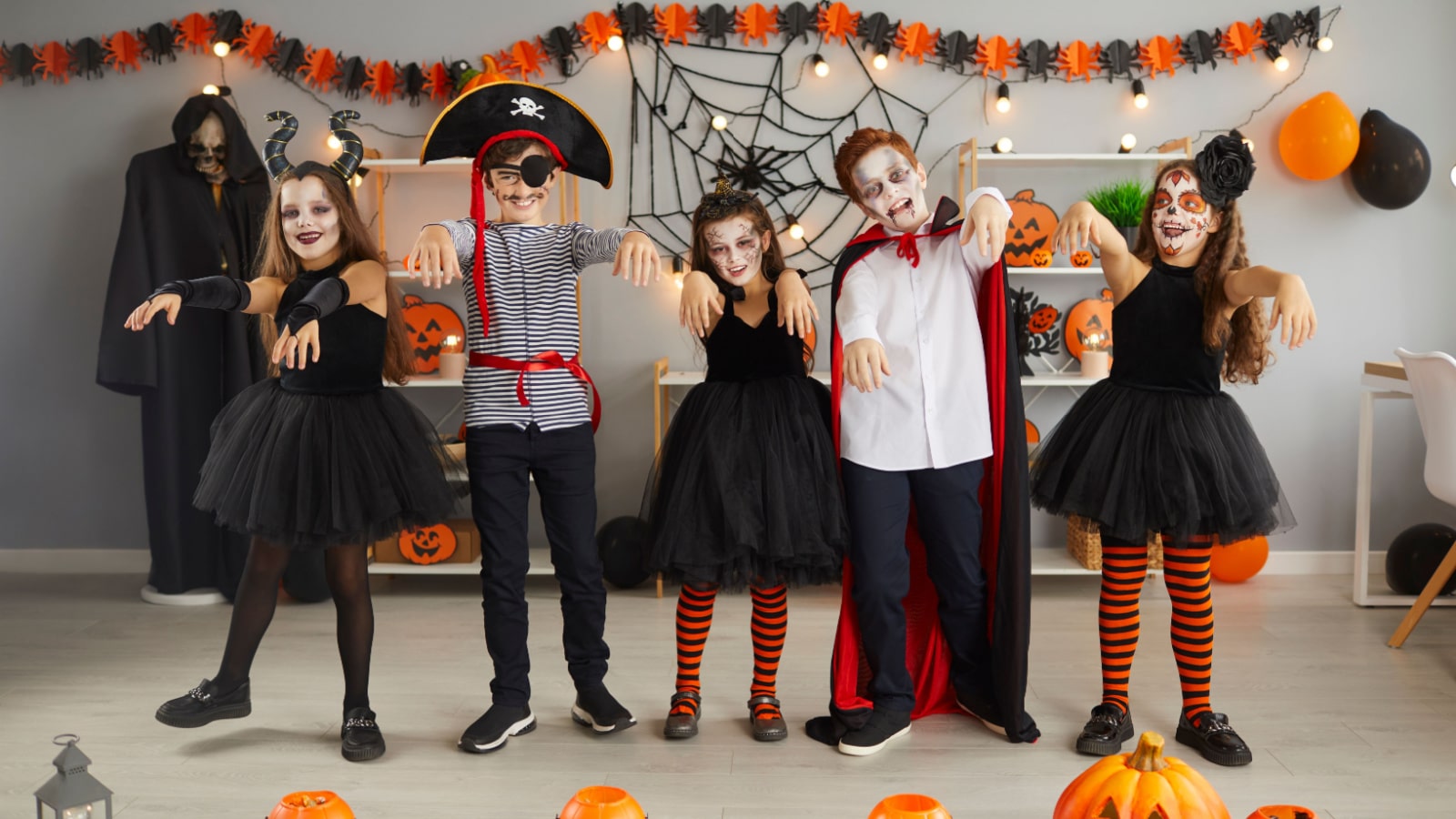 Group of children having fun and doing zombie dance at Halloween party at home. Bunch of happy kids dressed up in different spooky costumes walking and dancing like zombies in decorated living room