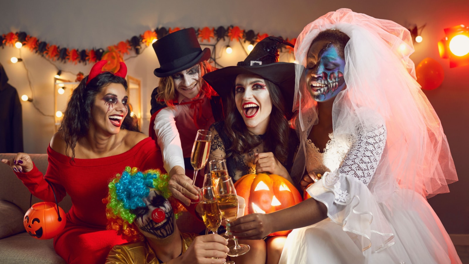 Cheers. Happy young people drinking and having fun at Halloween party. Multiracial group of excited adult friends disguised in spooky outfits sitting on sofa and raising flute glasses to spooky season