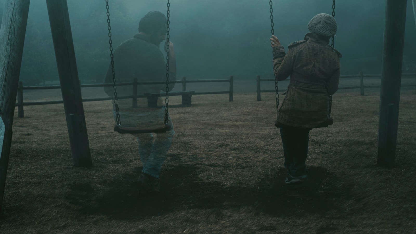 Concept of afterlife and memory for parents or lost love. Back view of woman sitting on a swing with ghost man near her outdoor in the park with fog. . Dead friend or husband concept. Life and death