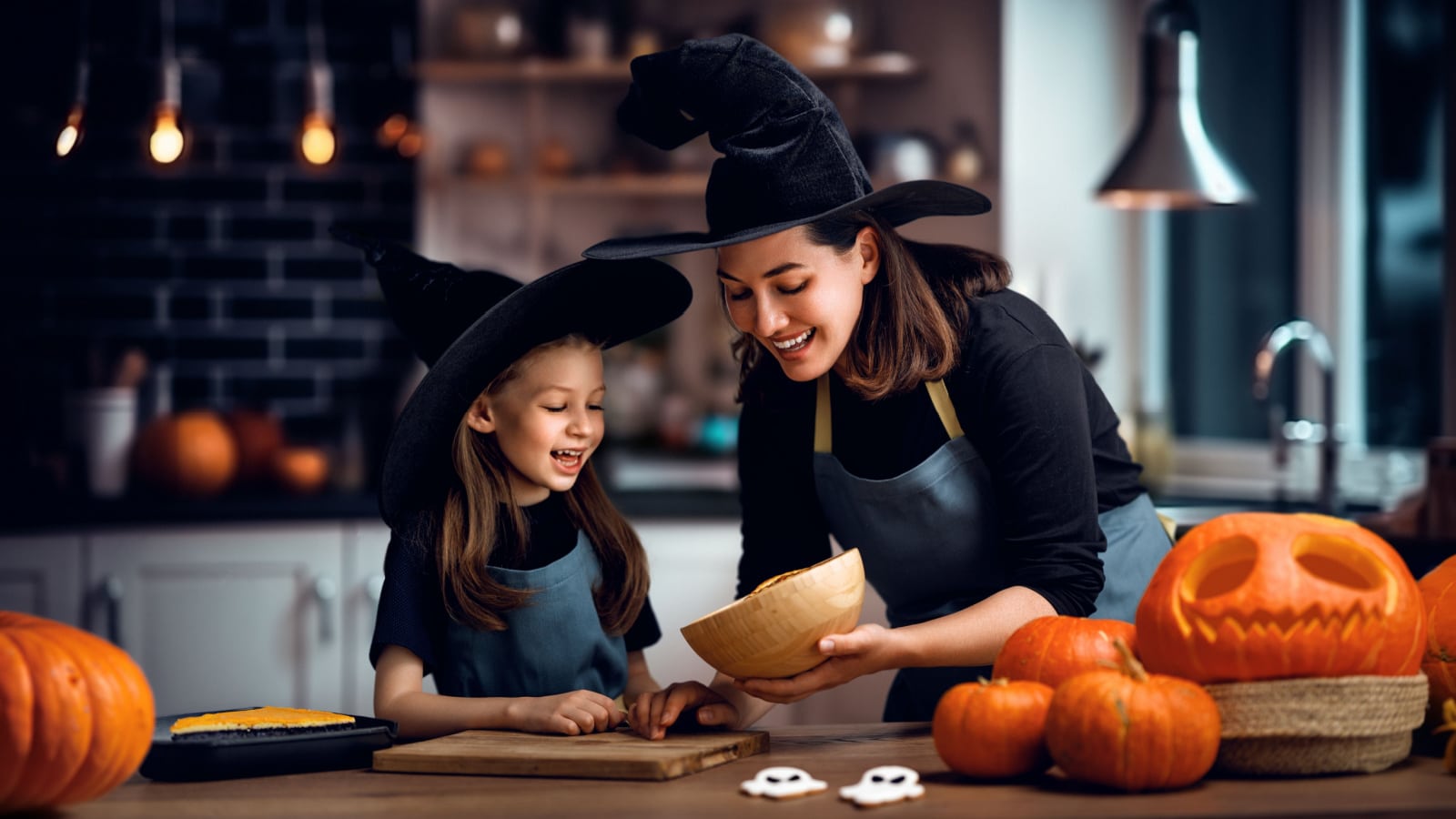 Mother and her daughter having fun at home. Happy Family preparing for Halloween. Mum and child cooking festive fare in the kitchen.