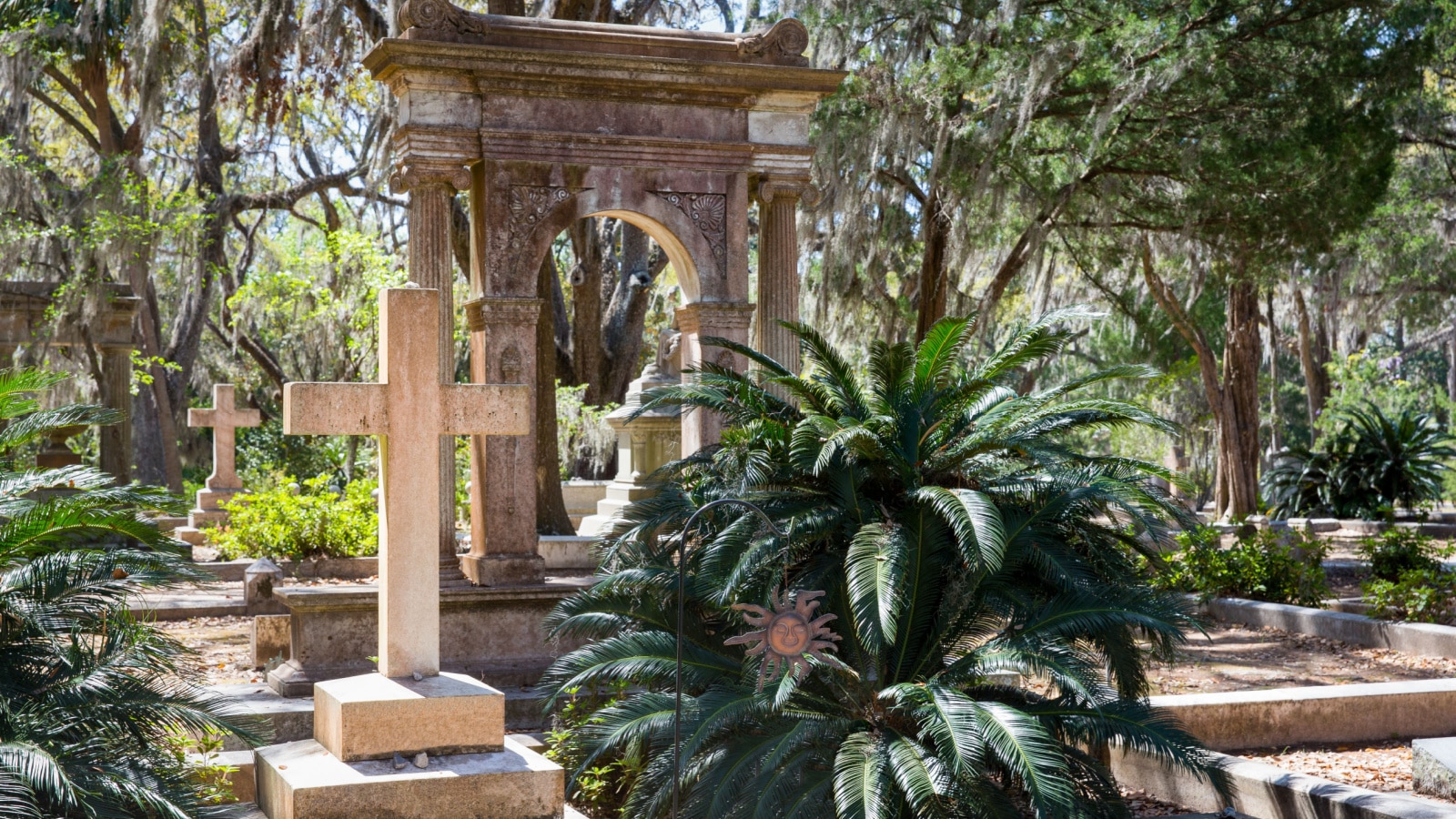 Historic Bonaventure Cemetery in Savannah, GA. Serene scene with prominent cross in the foreground, lush vegetation, and Spanish moss.