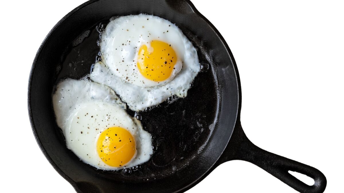 Two fried eggs in cast iron frying pan sprinkled with ground black pepper. Isolated on white from above.