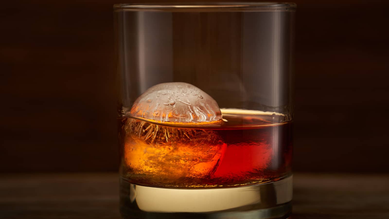 A glass of whisky with round big ice cube inside