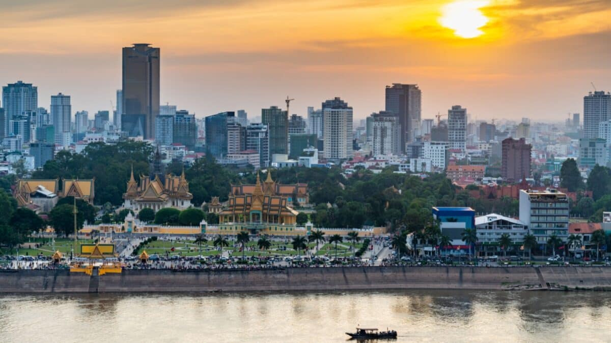 Rooftop view,looking across to the Riverside area of Cambodia's capital city.Sunset over Royal Palace and high rise buildings beyond, as a small boat drifts by towards the Mekong river.