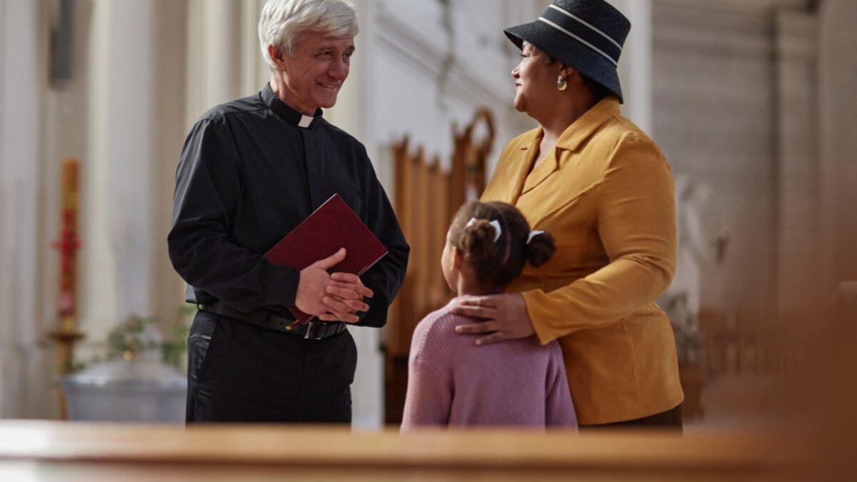 Senior priest discussing ceremony together with woman and her granddaughter while they visiting the old church