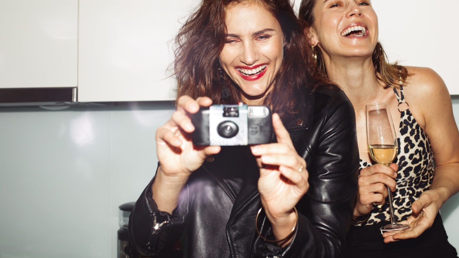 Cheerful women partying at home drinking wine. Woman taking a photo on a disposable camera at a house party.