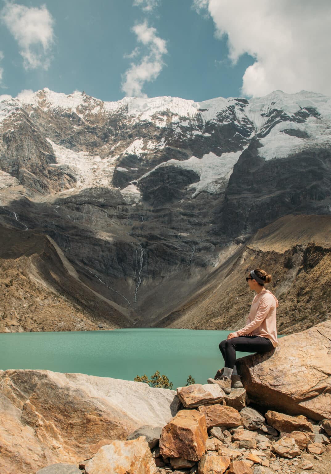 Lindsey looking at the bright blue Humantey Lake in Peru with mountains and a clear blue sky in the background