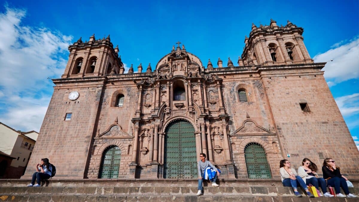 People sit on the steps of Cathedral Basilica of the Assumption of the Virgin or the Cusco Cathedral in Plaza de Armas in Cusco, Peru 