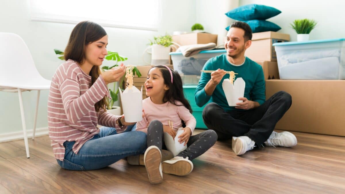 Attractive young woman feeding her cute daughter with chinese food. Happy family taking a break from unpacking and eating lunch together in moving day