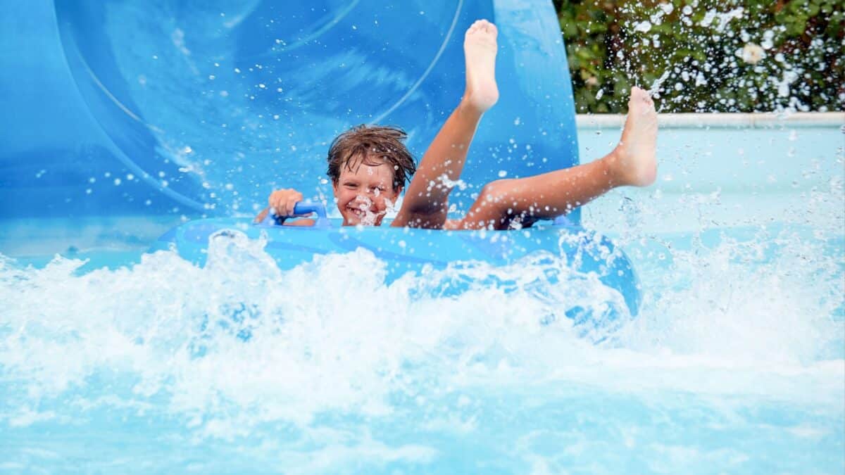 happy an 8 year old boy is riding in the water Park on inflatable circles on water slides with splash