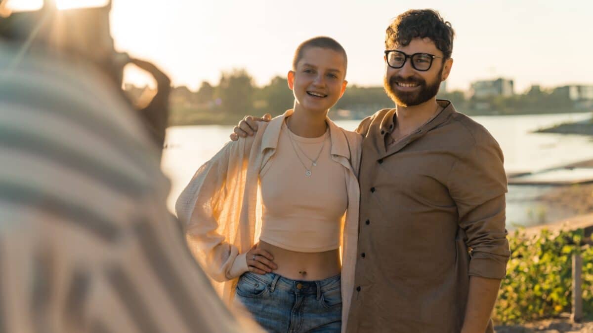 Photographer POV. Young caucasian couple asking someone to take their picture. Bald queer person in their 20s posing with caucasian bearded hipster guy