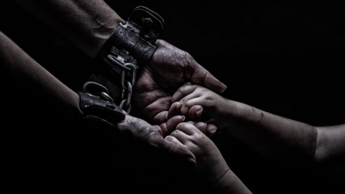 a woman in shackles holds a child by the hand on a black background