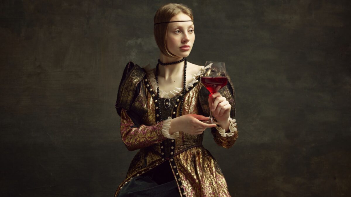 Portrait of pretty, young girl, princess in vintage dress drinking red wine against dark green background. Celebration, degustation. Concept of history,