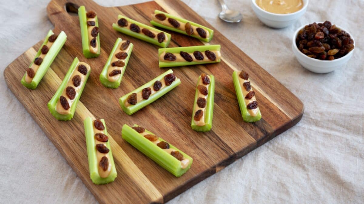 Homemade ants on a log with celery, peanut butter and raisins on a wooden board, side view.