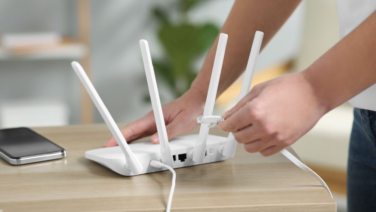 Woman inserting ethernet cable into Wi-Fi router at table indoors, closeup