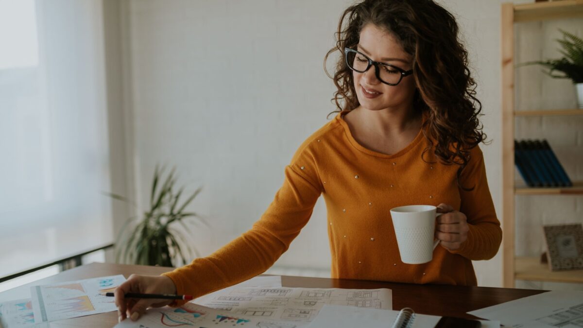 Beautiful young statistician is analyzing data while having coffee at office. Young business woman is enjoying her work.