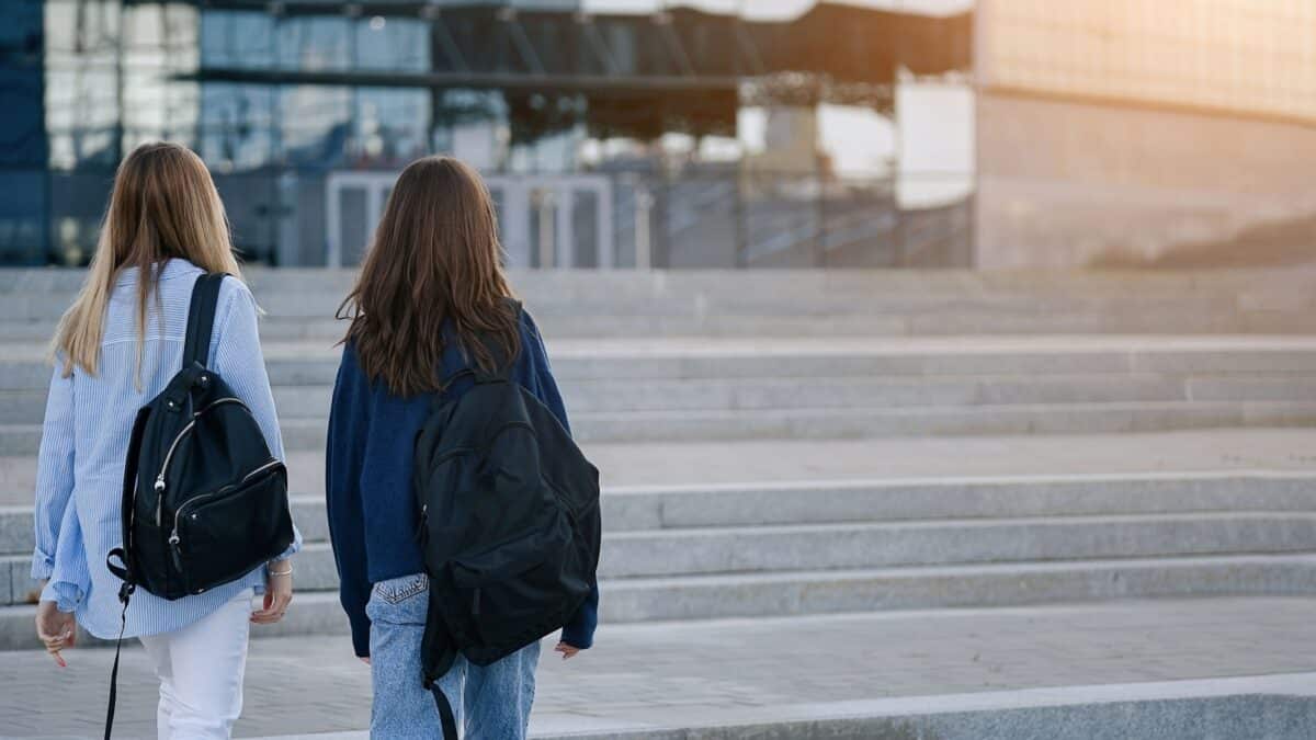 Two teenage student friends girls happy going to college or school. Back view