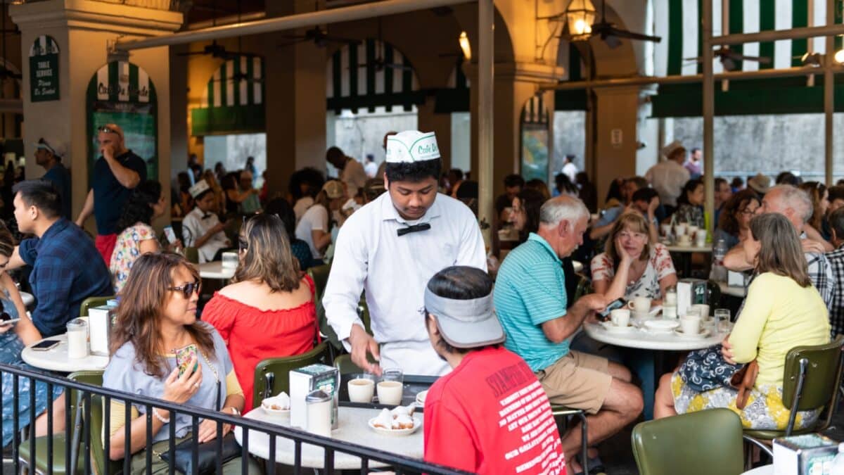 New Orleans, USA - April 22, 2018: People in Cafe Du Monde restaurant eating beignet powdered sugar donuts and chicory coffee served by waiter