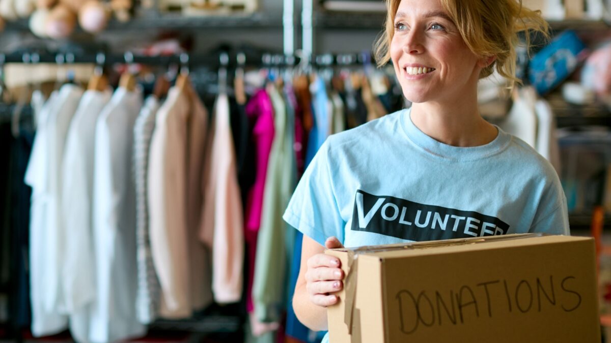 Female Charity Volunteer Holding Box Of Donations At Thrift Store Or Food Bank