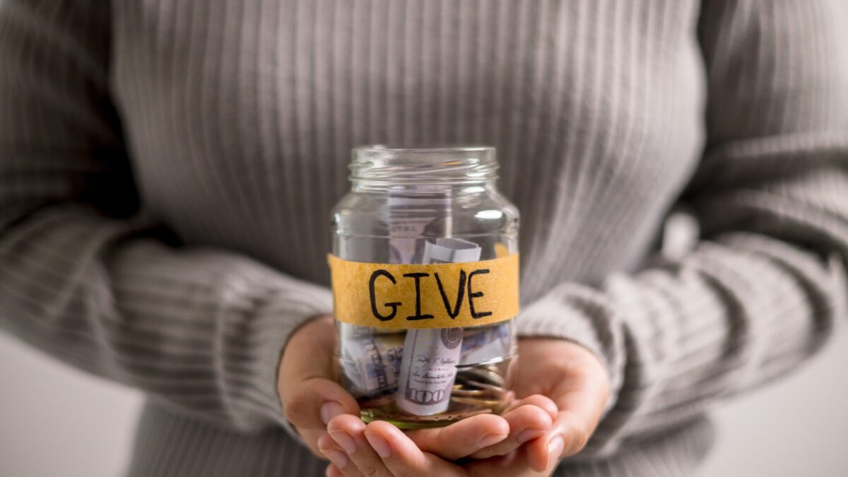 Woman holding coins and cash in jar with words Give or Donate elegantly lettered on its front, embodying spirit of giving. words, lettering, donate, jar, money, giving, woman, give, coin.